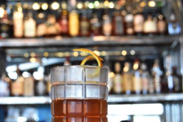 Repeal 18th bourbon bar with craft cocktail in foreground. Click to read article about Repeal 18th and Old Shawnee Pizza near North Kansas City's 18th & Clay Corridor, RiverNorth District